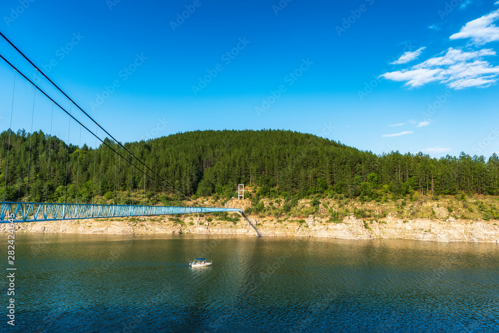 Fisherman boat crossing river under suspension bridge
