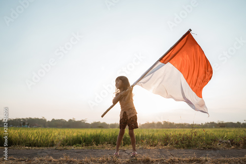 asian little girl flapping Indonesian flag with spirit in the rice field photo