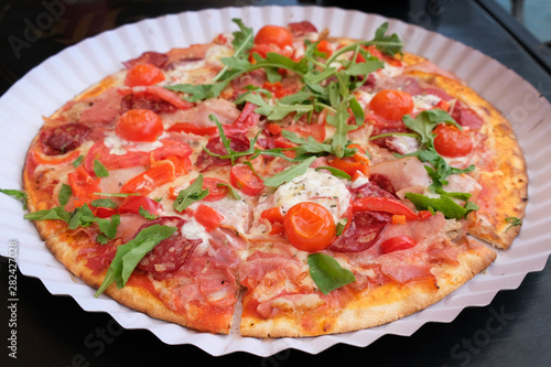 Pizza with cherry tomatoes, bacon, mozzarella and arugula top view. Round thin-crust pizza with vegetables and meat.