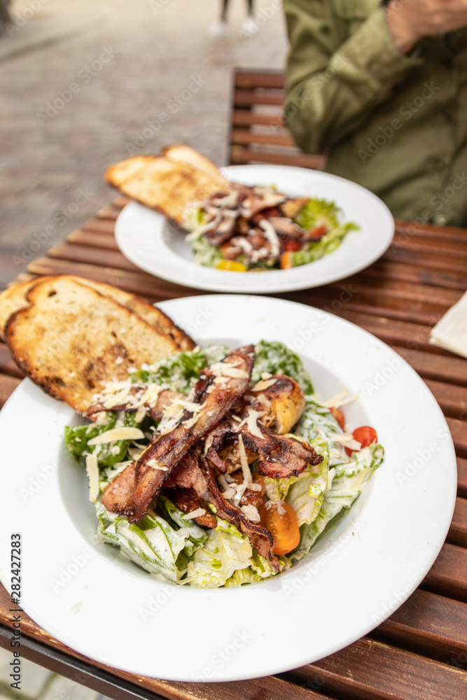 Close up of hands holding Caesar salad in restaurant. Tasty salad on white wooden table in cafe