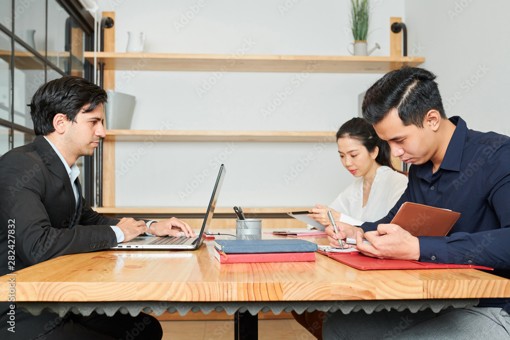 Group of business people sitting at the table working with documents and laptop computer during work day at office Group of business people sitting at the table working with documents and laptop computer during work day at office