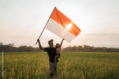 asian young father with daughter flapping Indonesian flag with spirit in the rice field photo