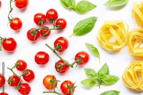 Cherry tomatoes with basil leaves and uncooked pasta tagliatelle nest on white background.