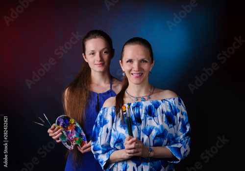 two artists with paints and brushes in hands over black background
