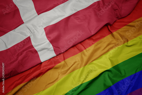 Photography waving colorful gay rainbow flag and national flag of denmark.