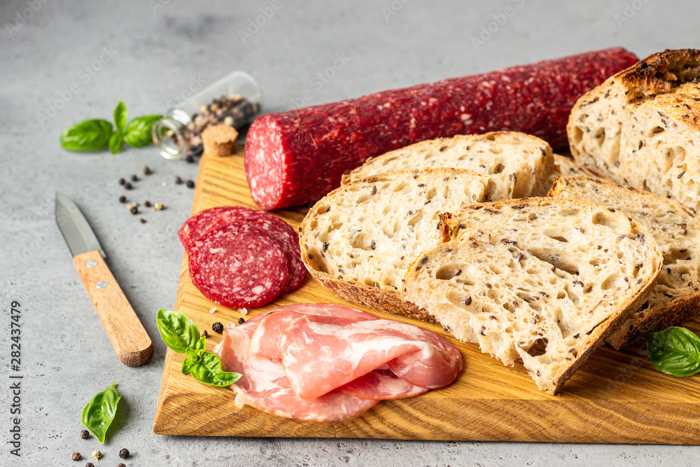 Traditional artisan bread with seeds and pork sausage and salami served on a wooden cutting board. Open sandwich with pork sausage.