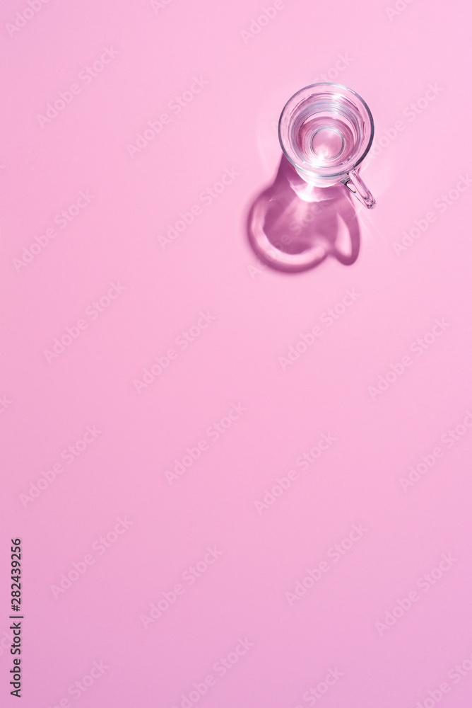 Glass cup filled with clear water on a pink background. Top view.