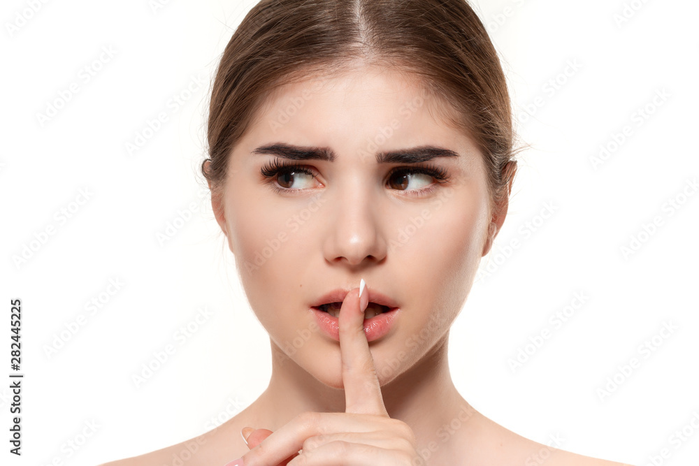 Close-up portrait of a beautiful young girl holding finger near her mouth expressing idea of secret isolated over white background. Close-up portrait of a beautiful young girl holding finger near her mouth expressing idea of secret isolated over white background.