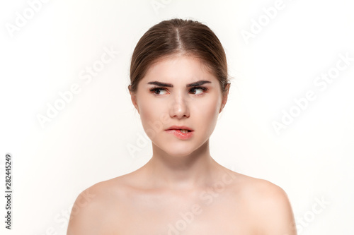 Close-up portrait of a beautiful young girl biting lips with cunning look isolated over white background.