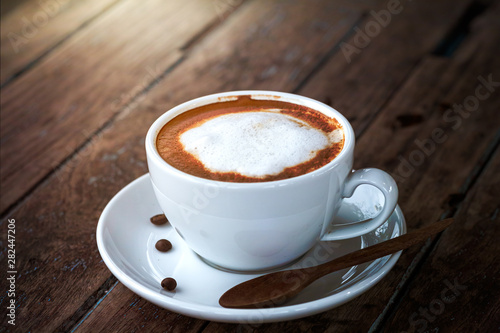 a white cup of black coffee with latte art serving on wooden table in natural light