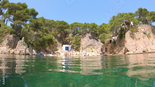 Spain, small beach on rocky coast with tourists in summer vacations, seen from water surface, Mediterranean sea, Costa Brava, Aigua Xelida, Palafrugell, Catalonia photo