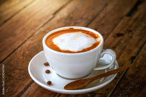 a white cup of hot coffee with latte art serving on brown wooden table in natural daylight