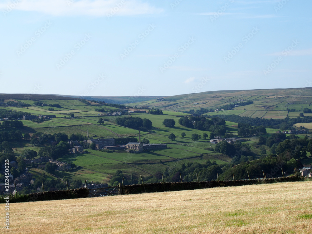Naklejka premium a scenic view of west yorkshire countryside with the village of luddenden at the bottom of the calder valley with buildings surrounded by farms and fields