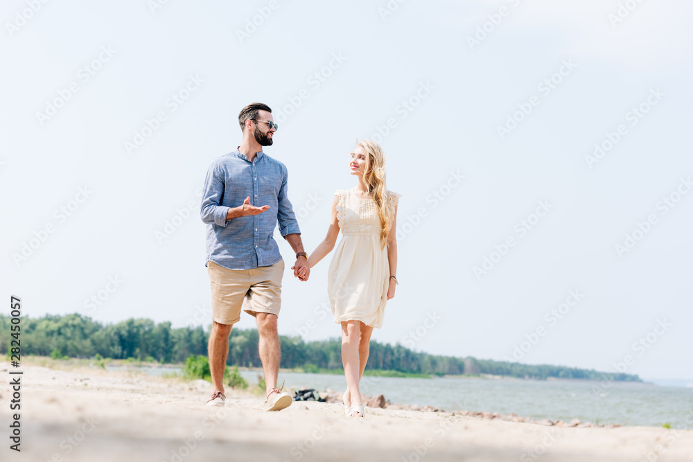 adult couple walking along beach, talking and holding hands adult couple walking along beach, talking and holding hands