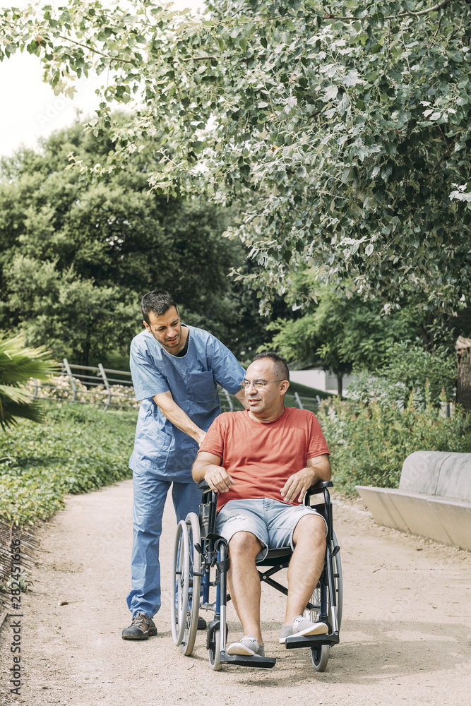man in wheelchair talking with his nurse at park man in wheelchair talking with his nurse at park