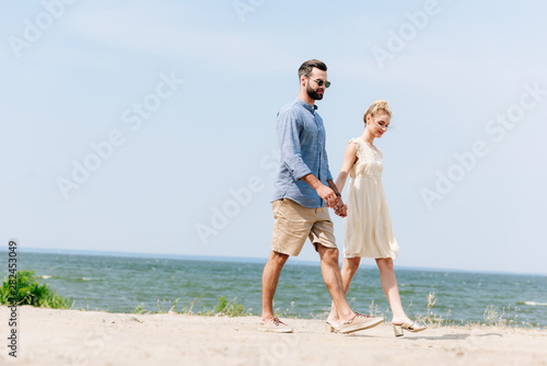 adult couple walking along sandy beach and holding hands