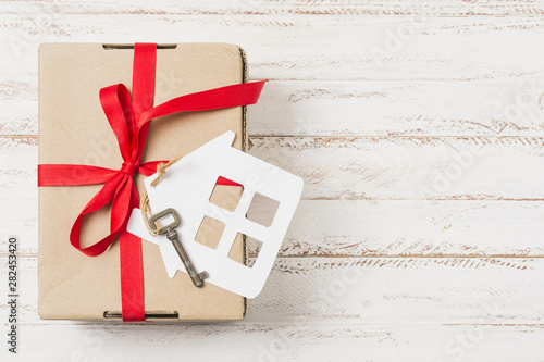фотографія High angle view of a gift box tied with red ribbon on house key over wooden tabl