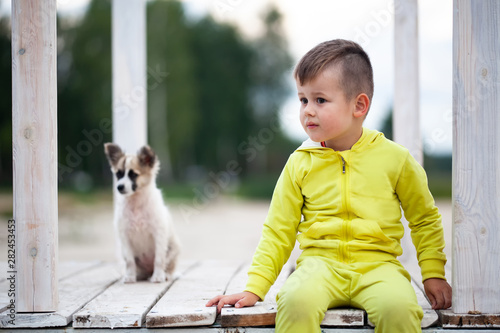 Cute little boy sitting on footbridge with his dog. Protection of animals.