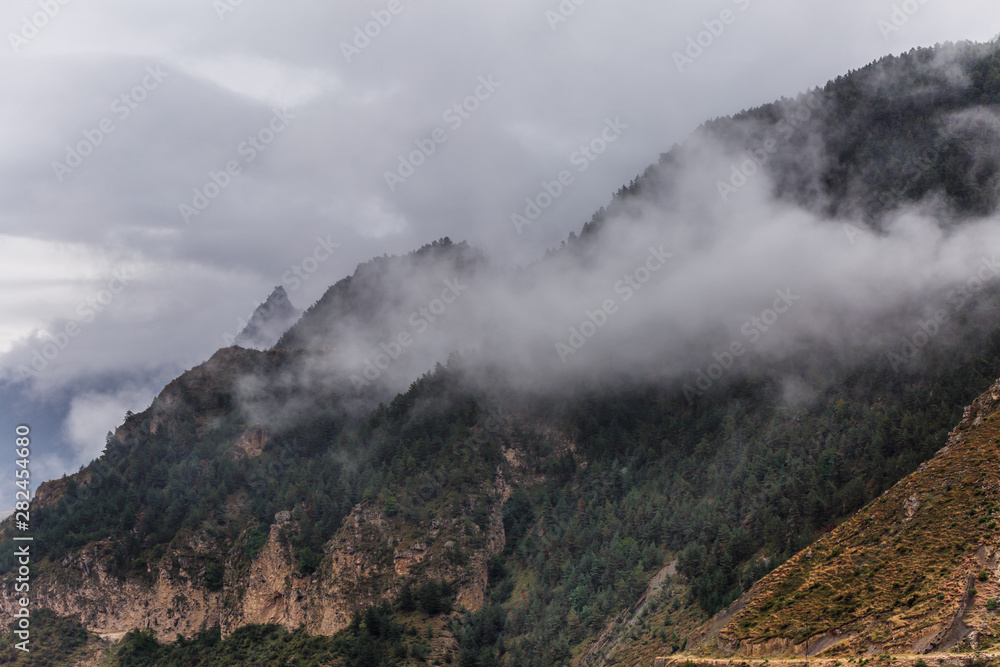 Image of mountains with trees, smoke, gray sky