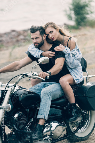 young couple of bikers hugging on black motorcycle at sandy beach
