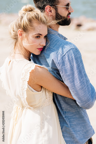Murais de parede young blonde woman hugging bearded boyfriend at beach