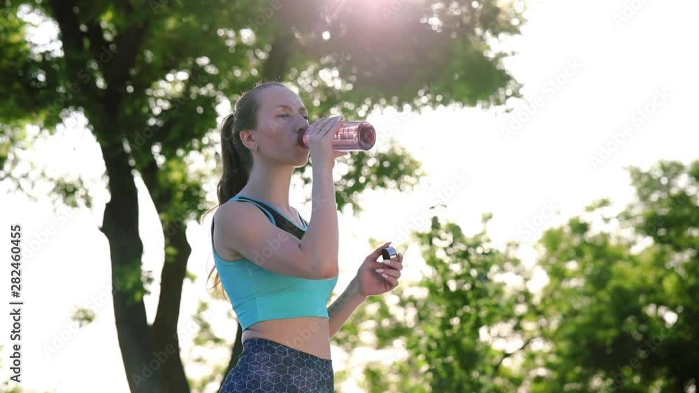 relaxed young woman with dark ponytail holds plastic bottle and drinks water after hard workout close view slow motion