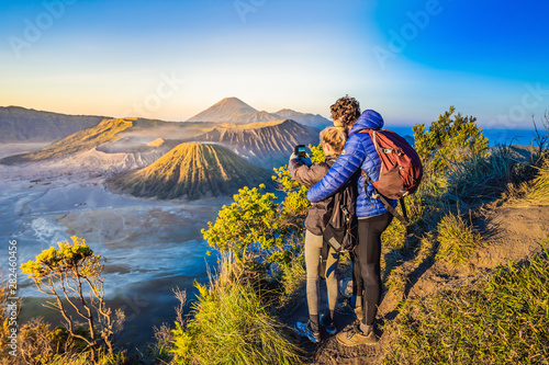 Young couple man and woman meet the sunrise at the Bromo Tengger Semeru National Park on the Java Island, Indonesia. They enjoy magnificent view on the Bromo or Gunung Bromo on Indonesian, Semeru and