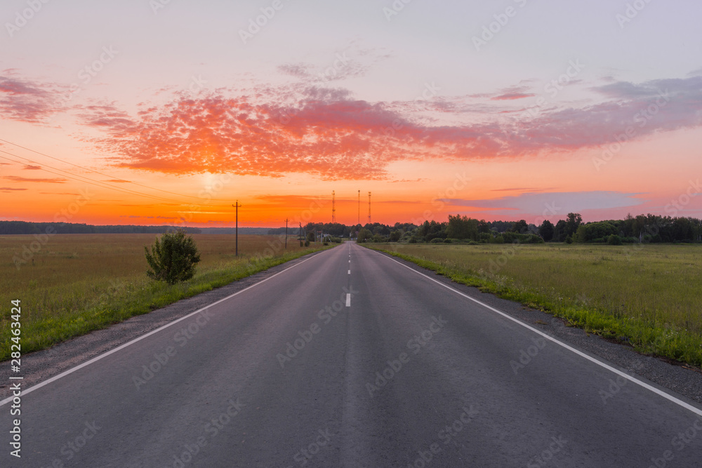 Direct asphalt road in the middle of a wheat field illuminated by a beautiful sunrise