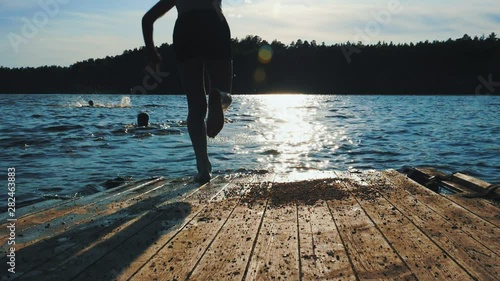 A teenager jumps from a dock into river water. Sunny summer day. Sunset time. Slow motion.