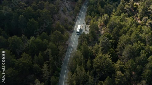 Aerial drone shot of white tourist bus driving at mountain forest road in Cyprus Troodos. Left hand traffic.