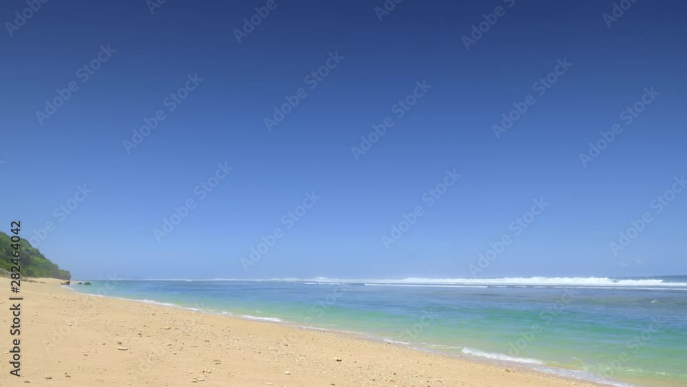 Sunny tropical beach with yellow sand and stones and beautiful colorful ocean with big tide waves near reef Sunny tropical beach with yellow sand and stones and beautiful colorful ocean with big tide waves near reef
