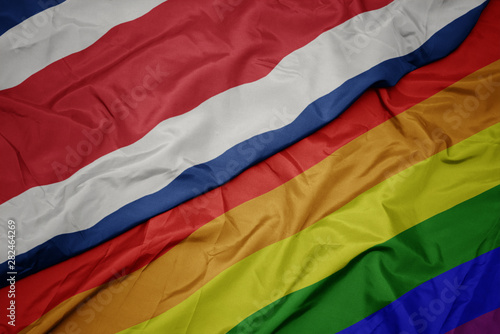 waving colorful gay rainbow flag and national flag of costa rica.