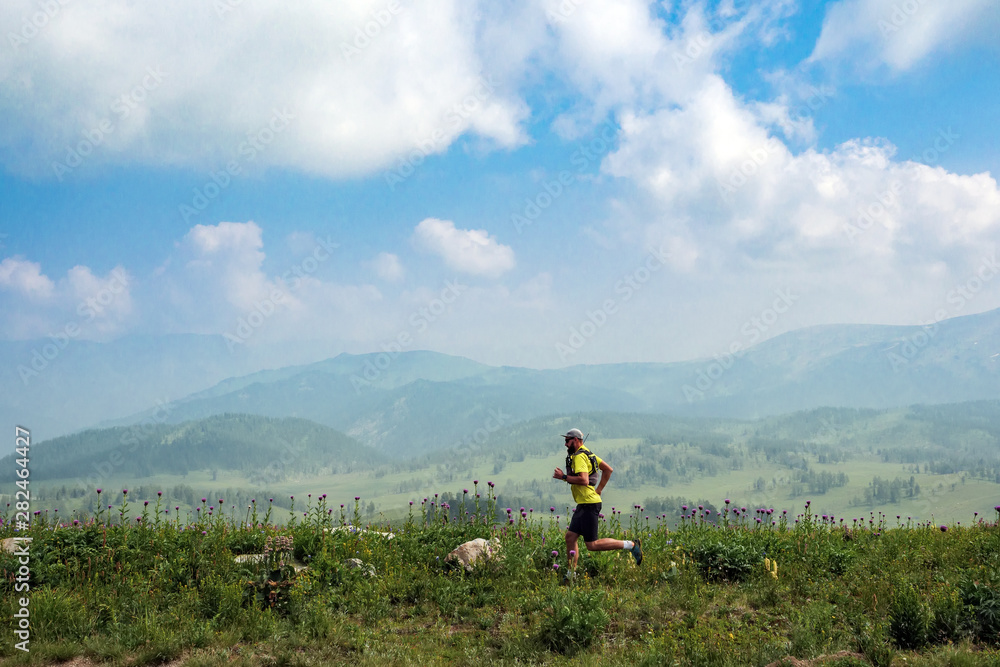 Athlete runs along a flowering meadow in highlands. Man in a yellow T-shirt and black shorts is training in outdoors. Trail running Athlete runs along a flowering meadow in highlands. Man in a yellow T-shirt and black shorts is training in outdoors. Trail running