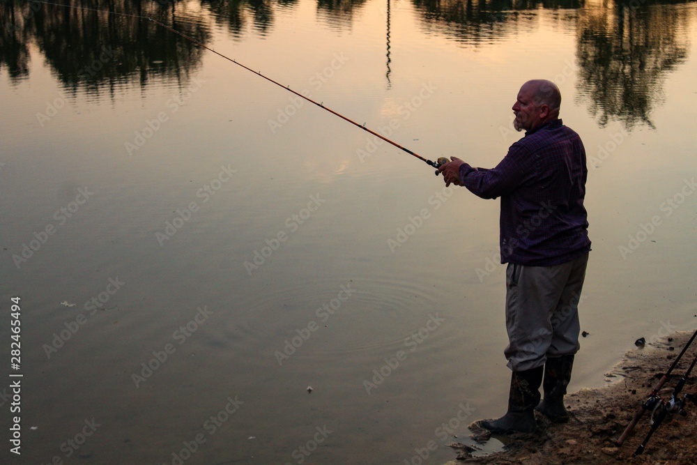 Peaceful Scene of Middle Aged Man Fishing on a Country Pond at Sunset with Golden filtered light reflected on pond Peaceful Scene of Middle Aged Man Fishing on a Country Pond at Sunset with Golden filtered light reflected on pond