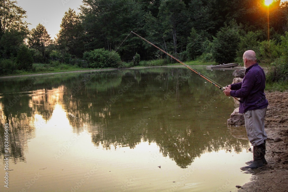 Peaceful Scene of Middle Aged Man Fishing on a Country Pond at Sunset with Golden filtered light reflected on pond Peaceful Scene of Middle Aged Man Fishing on a Country Pond at Sunset with Golden filtered light reflected on pond
