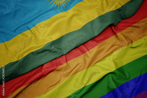 waving colorful gay rainbow flag and national flag of rwanda.