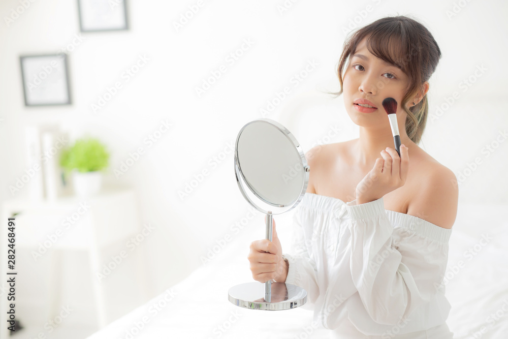 Beauty portrait young asian woman smile with face looking mirror applying makeup with brush cheek in the bedroom, beautiful of girl holding blusher, skin care and cosmetic concept. Beauty portrait young asian woman smile with face looking mirror applying makeup with brush cheek in the bedroom, beautiful of girl holding blusher, skin care and cosmetic concept.