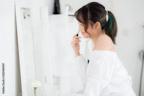 Beauty portrait young asian woman smile with face looking mirror applying makeup with brush cheek in the bedroom  beautiful of girl holding blusher  skin care and cosmetic concept.