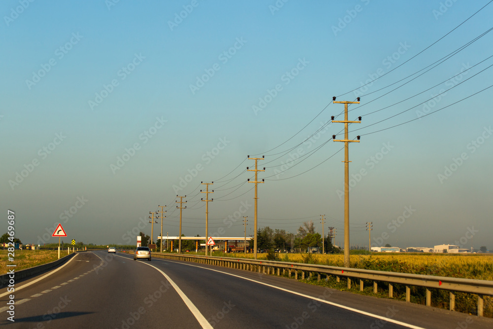 Perspective shot of concrete electric poles and wires near to highway on rural area. Morning day light creates warm atmosphere.
