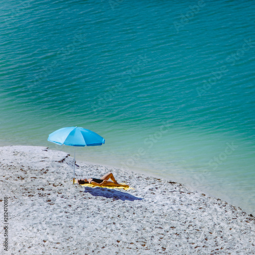 woman in swimsuit walking by sand beach blue sun umbrella and yellow blanket