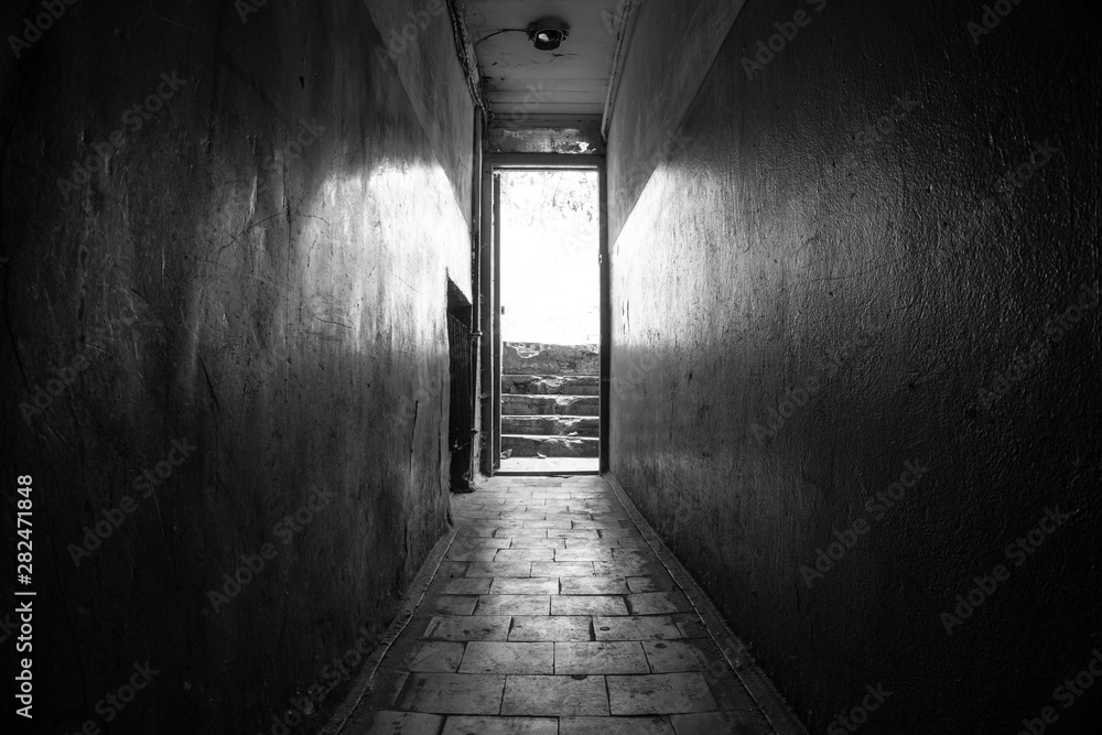 Empty dark corridor with light at the end. You can reach it by stairs.