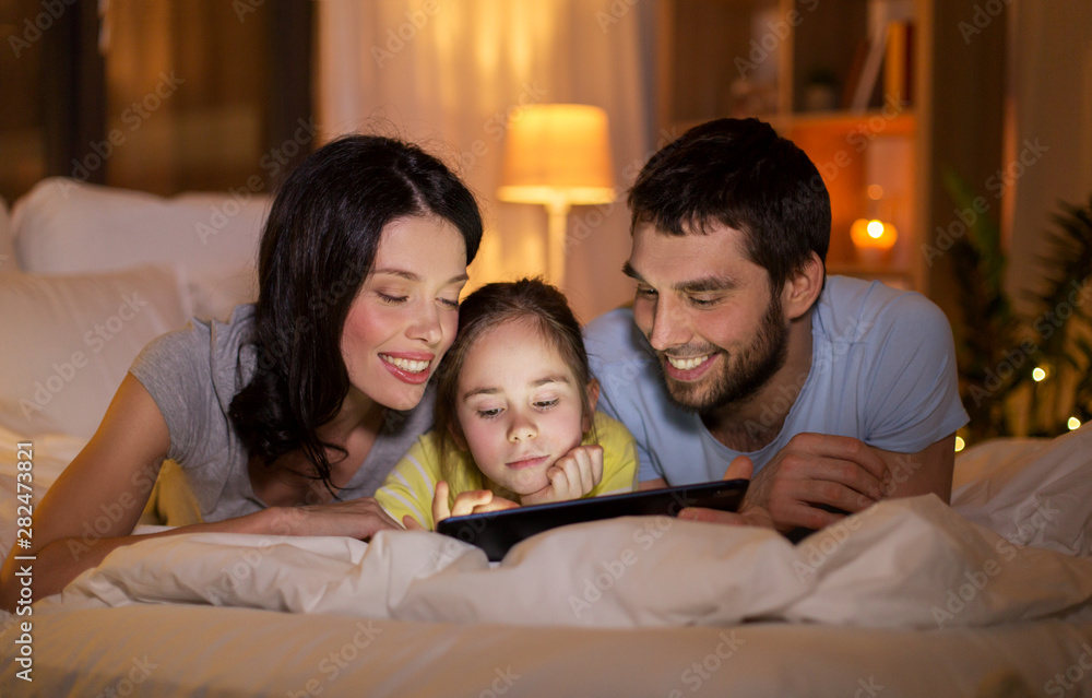 people and family concept - happy mother, father and little daughter with tablet pc computer in bed at night at home