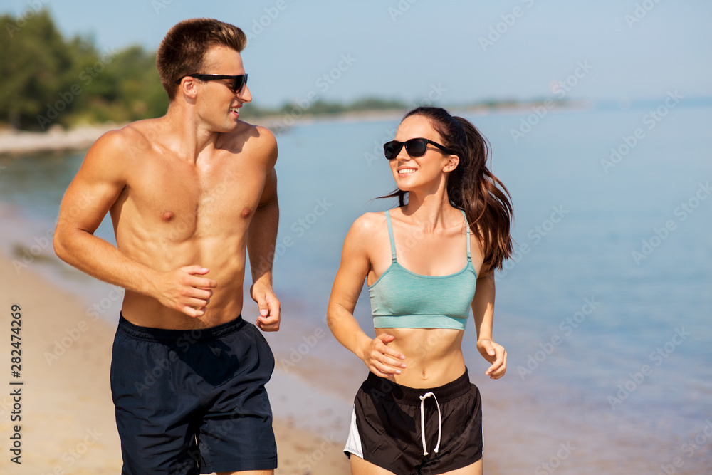fitness, sport and lifestyle concept - happy couple in sports clothes and sunglasses running along summer beach fitness, sport and lifestyle concept - happy couple in sports clothes and sunglasses running along summer beach