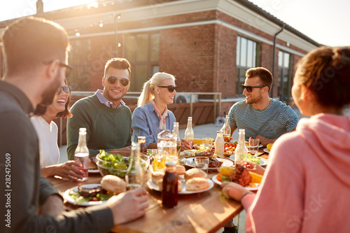 leisure and people concept - happy friends having dinner or barbecue party on rooftop in summer