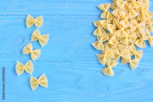 Traditional italian farfalle pasta with selective focus on blue textured wooden background. Bow tie noodles on wood backdrop. Raw organic farfalle noodle. Uncooked dried homemade farfalle. Butterfly  photo