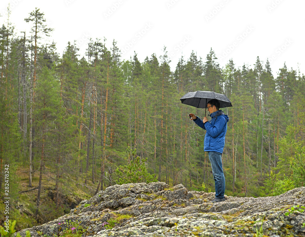 Φωτογραφία Young man with black umbrella stands in pouring rain on rock and takes photos of nature
