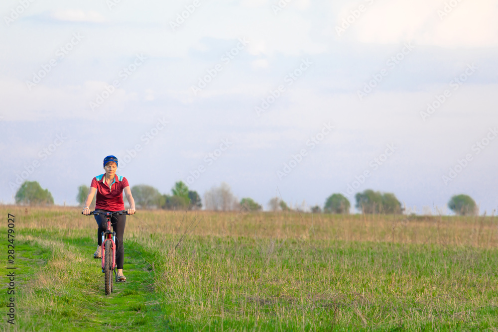 Girl on a bicycle on a background of blue sky and green grass