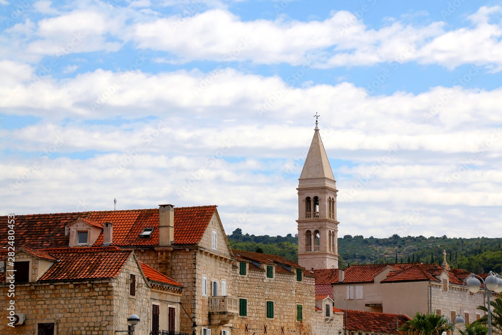Fototapeta premium Traditional stone architecture and landmark Church of Mary's Annunciation bell tower in small town Supetar, on island Brac, Croatia.