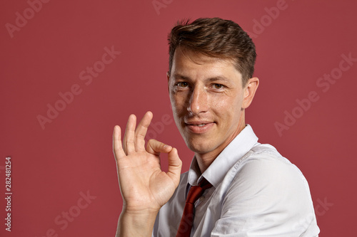 Young man in a classic white shirt and red tie posing over a pink background.