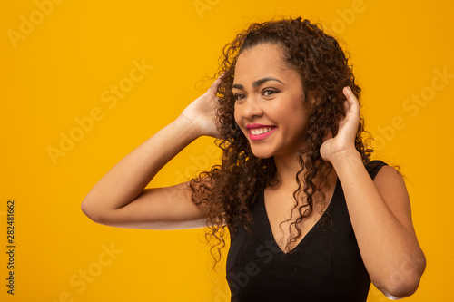 Beautiful young woman with curly hair on yellow background